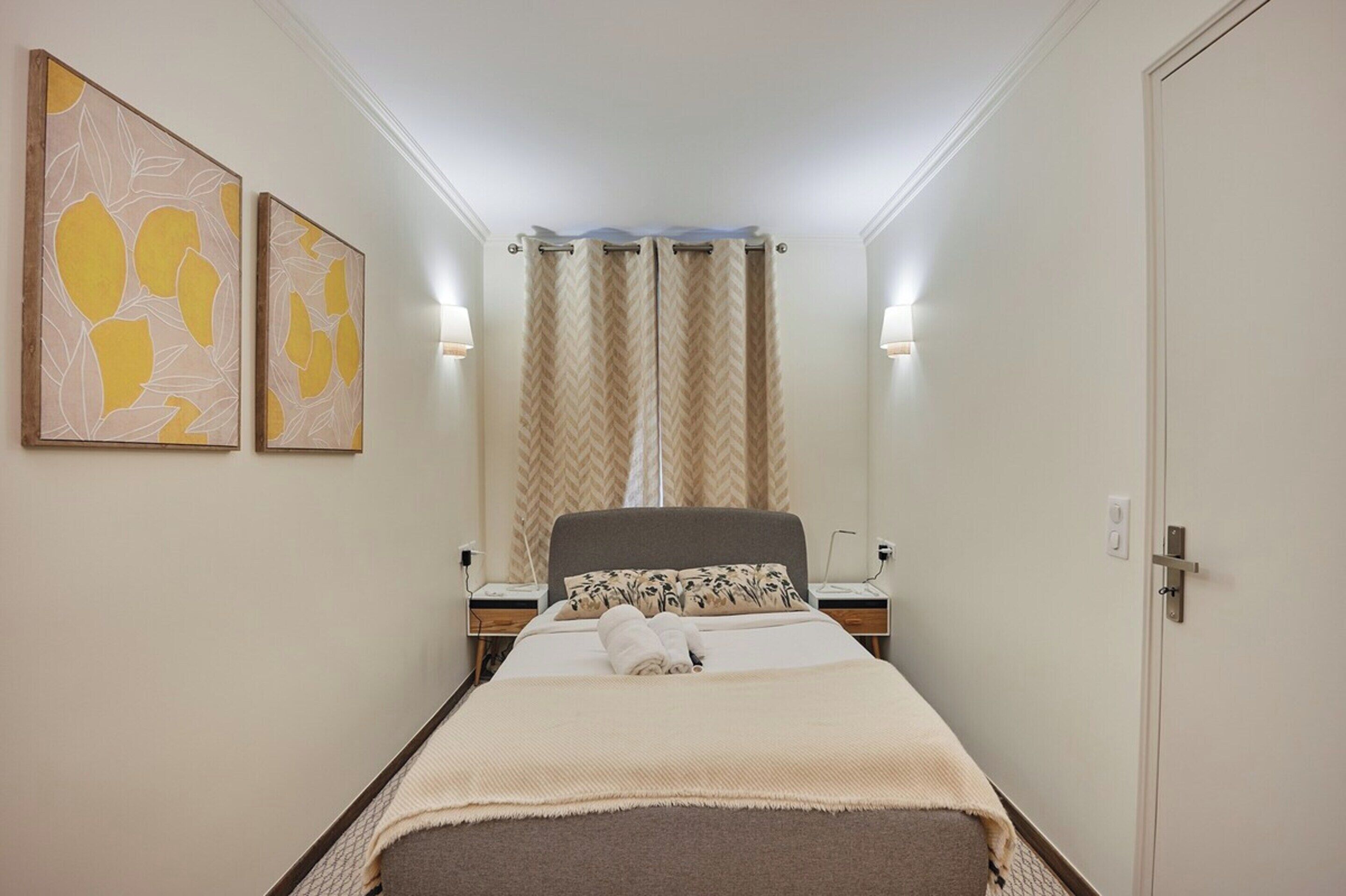 A hotel room with a bed, two bedside tables, a nightstand, a lamp, a door, and a window with curtains.