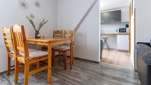 A dining area with a wooden table and chairs, a small plant, and a view into a kitchen with modern appliances. - Ferienwohnung in Busum (Büsum)