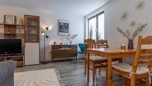 A modern living room with a flat-screen TV, wooden dining table, and chairs, a blue armchair, and a wooden cabinet with glass doors. - Ferienwohnung in Busum (Büsum)