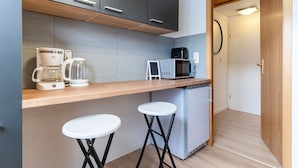 A compact kitchen with a microwave, coffee maker, and a small refrigerator. There are two stools and a wooden countertop. - Ferienwohnung in Busum (Büsum)