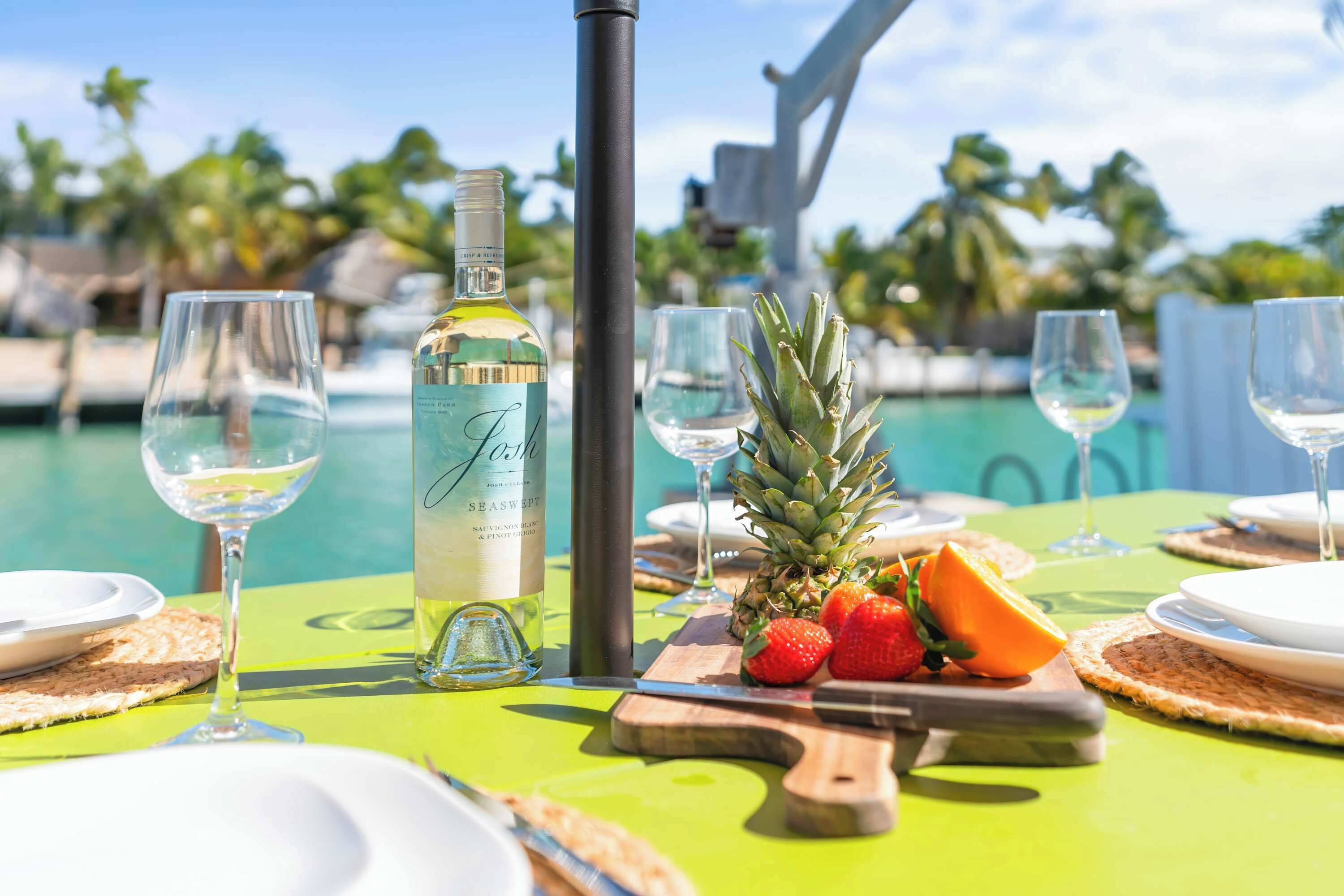 A table set for a meal with a bottle of wine, plates, cutlery, and tropical fruits.