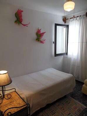 Una habitación con cama, lámpara colgante, espejo y ventana con cortinas.