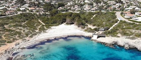 Vista aérea de una zona costera con playa, aguas turquesas cristalinas y una zona residencial con casas.
