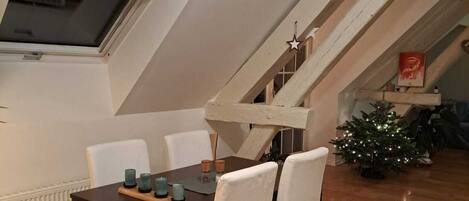 A dining area with a wooden table and white chairs, a small Christmas tree, and a staircase.