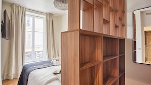 Une chambre à coucher avec un lit, une armoire en bois, une fenêtre avec des rideaux et un balcon.