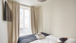 Une chambre à coucher avec un lit, un téléviseur fixé au mur et une fenêtre avec des rideaux.
