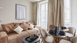 Un salon moderne avec un canapé marron, une table ronde entourée de chaises et une fenêtre avec des rideaux.