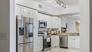 Una cocina moderna con muebles blancos, electrodomésticos de acero inoxidable y encimera de granito.