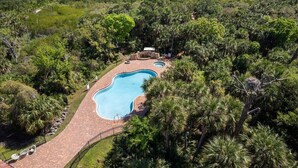 Una piscina grande y de forma irregular bordeada por un camino pavimentado, con abundante vegetación tropical y vistas al océano de fondo.