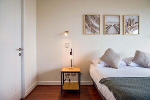 Een slaapkamer met een bed, een nachtkastje met een lamp en drie ingelijste foto’s aan de muur.