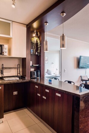 A modern kitchen with dark wood cabinets, a granite countertop, a built-in microwave, and a coffee maker.