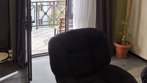 A modern living room with a black sofa, a wooden coffee table, and a potted plant. A sliding glass door leads to an outdoor balcony.