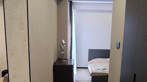 A narrow hallway leading to a bedroom with a bed, a nightstand, and a lamp.