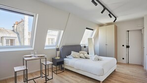 A bedroom with a bed, a small table, two chairs, a desk, and a wardrobe. There are two windows providing natural light. - Sublim Studio Beaubourg/le Marais (Paris)