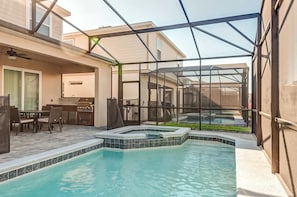 Uma piscina ao ar livre com hidromassagem, um terraço coberto e vista para uma casa ao fundo.