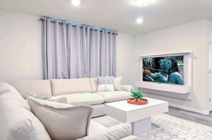 Uma sala de estar moderna com um sofá seccional, uma TV de tela plana na parede e uma mesa de centro com uma planta.