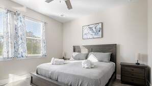 Ein Schlafzimmer mit einem großen Bett, einem Nachttisch, einem Deckenventilator und einem Fenster mit Vorhängen.