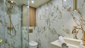 Une salle de bain moderne avec une douche à parois de verre, des toilettes blanches et un lavabo doté d’un robinet doré.