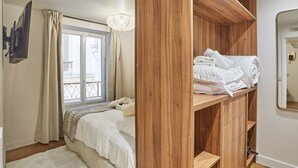 Une chambre à coucher avec un lit, une armoire en bois, une fenêtre avec des rideaux et un miroir.
