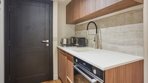 Une cuisine de taille réduite avec une porte sombre, des armoires en bois, un plan de travail blanc, un évier en acier inoxydable et un four encastré.