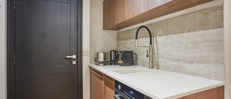 A compact kitchen with a dark door, wooden cabinets, a white countertop, a stainless steel sink, and a built-in oven.