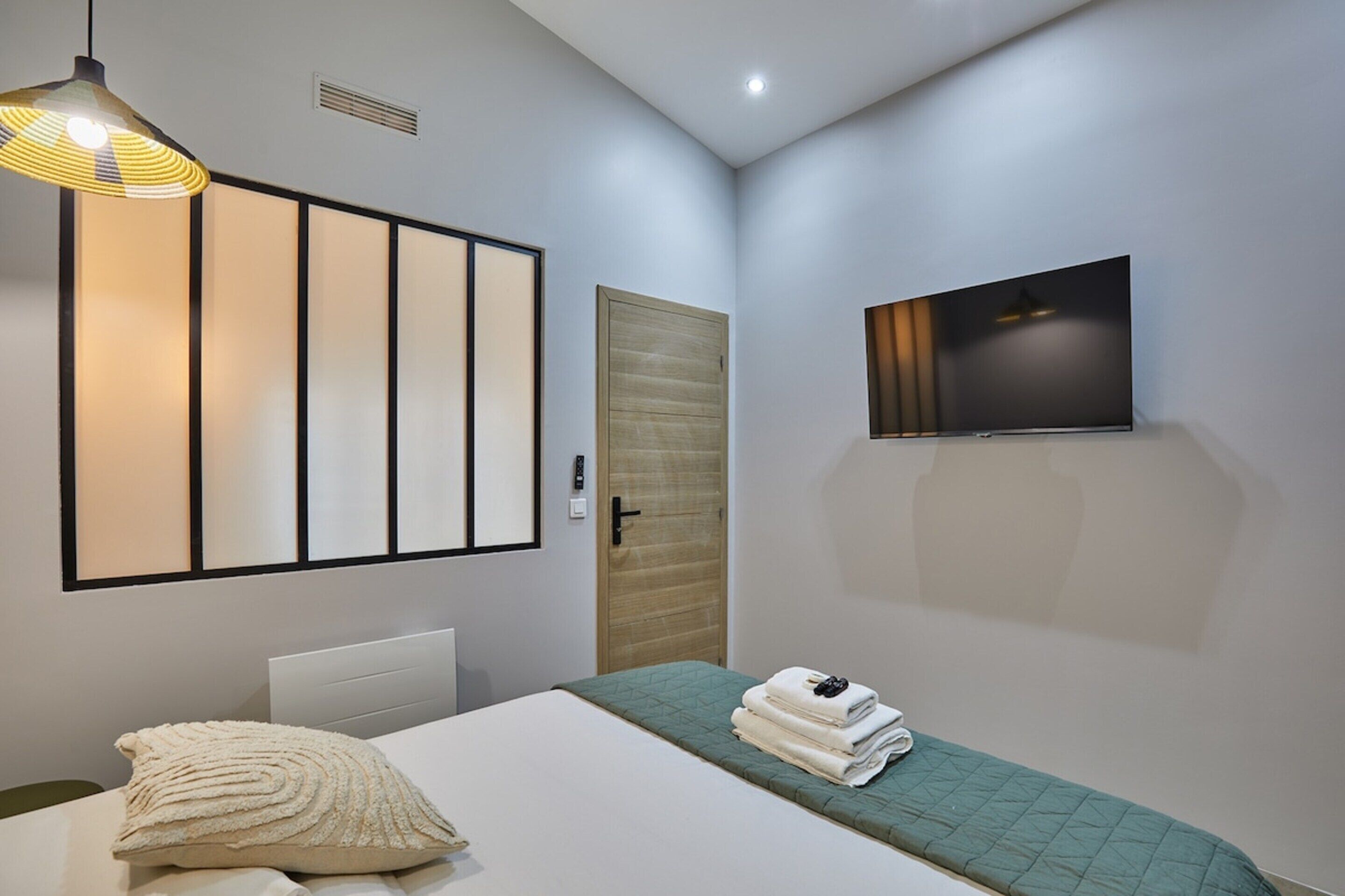 A modern bedroom with a bed, a TV mounted on the wall, a wooden door, and a ceiling light fixture.