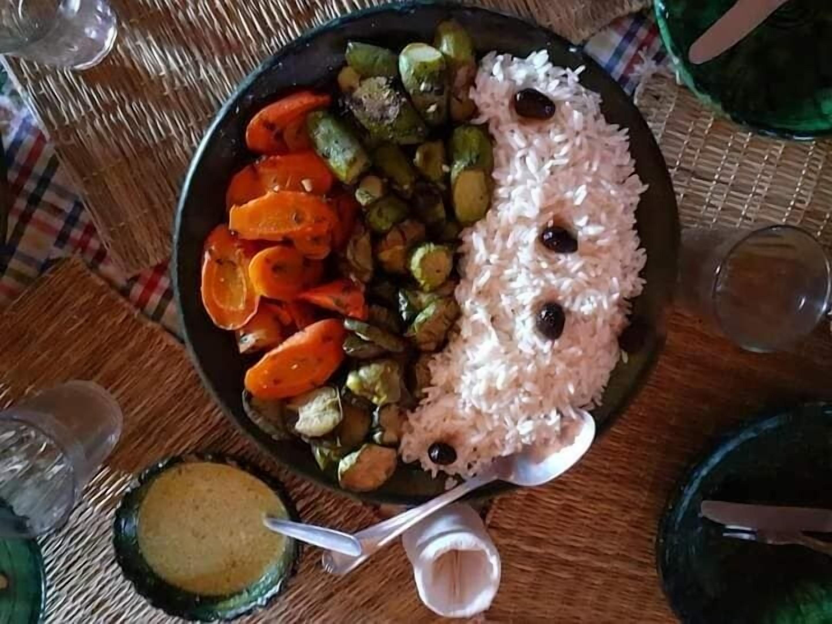 A plate of food with rice, carrots, and green vegetables on a table.