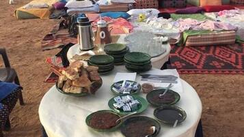 A desert setting with a table displaying various food items and textiles.