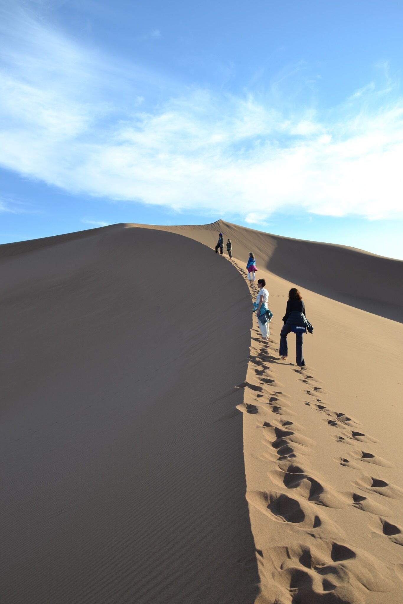 A desert landscape with sand dunes and footprints leading up the slope.