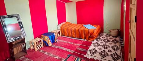A bedroom with a bed, a small table, a mirror, and a red and white striped wall.