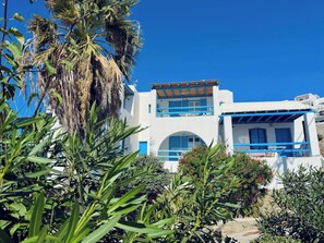 Ein weißes Gebäude mit blauen Akzenten, einem Balkon und üppigem Grün im Vordergrund.