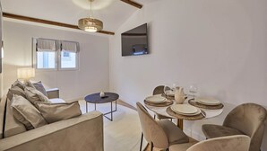 A modern living room with a sofa, a dining table set for four, and a television mounted on the wall. - Superb Apartment in the Heart of Paris (Paris)