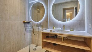 A modern bathroom with a glass-enclosed shower, a wooden vanity with a sink, and two large mirrors with circular frames. - Superb Apartment in the Heart of Paris (Paris)