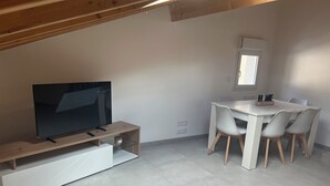 Un espacio habitable moderno con un televisor de pantalla plana sobre un soporte de madera, una mesa de comedor con cuatro sillas y un ventanal.