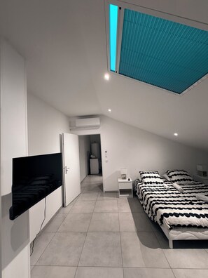 Une chambre moderne avec un plafond en pente, un lit avec une literie à pois, une table de chevet avec une lampe et un téléviseur fixé au mur.