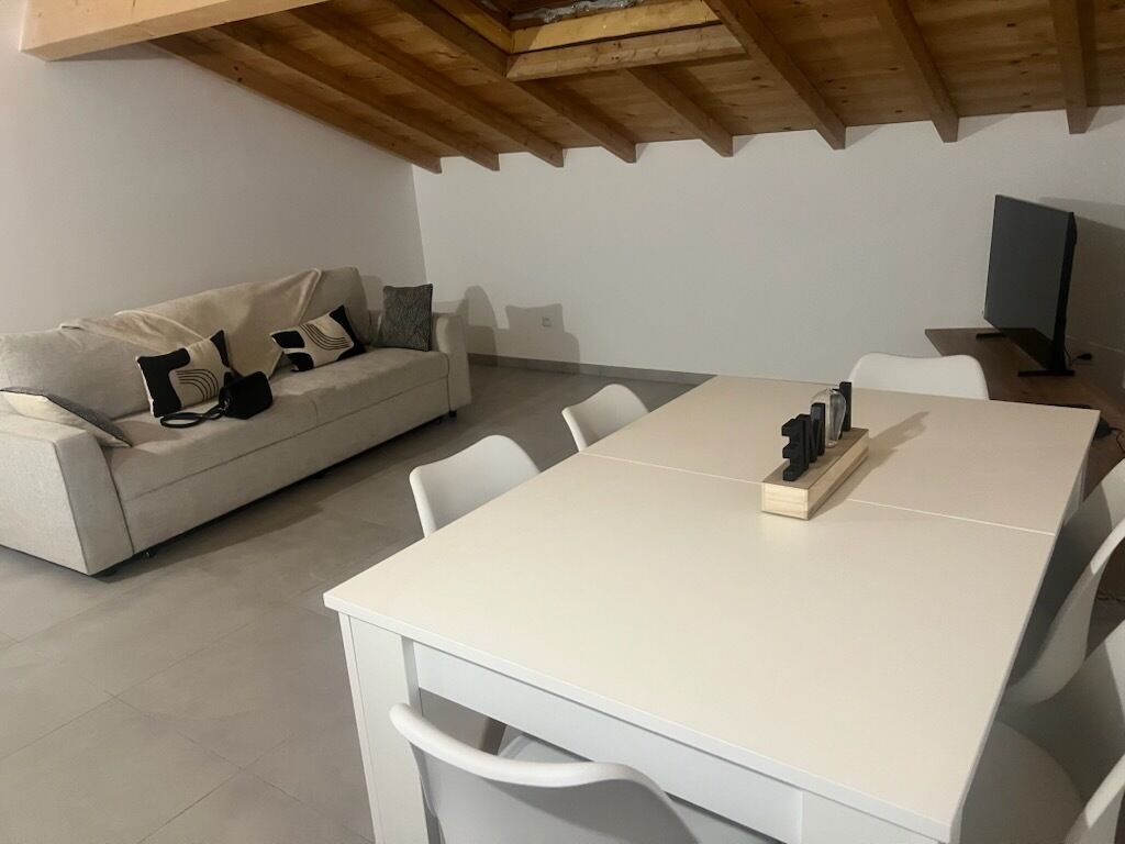 A modern living room with a white sofa, a dining table with chairs, and a wooden ceiling.