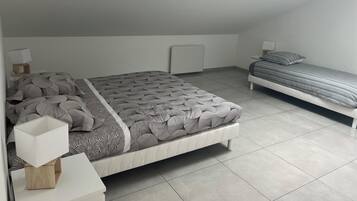 Een moderne slaapkamer met een schuine wand, een groot bed met een beddeken met een patroon, een kleiner bed, nachtkastjes met lampen en een dakraam.