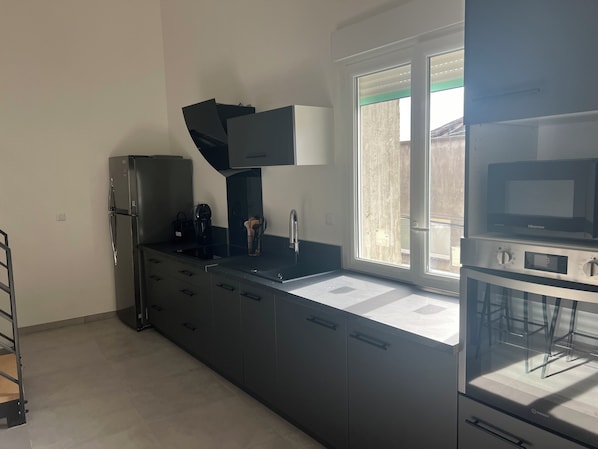 Una cocina moderna con encimera negra, electrodomésticos de acero inoxidable y ventana con vistas.