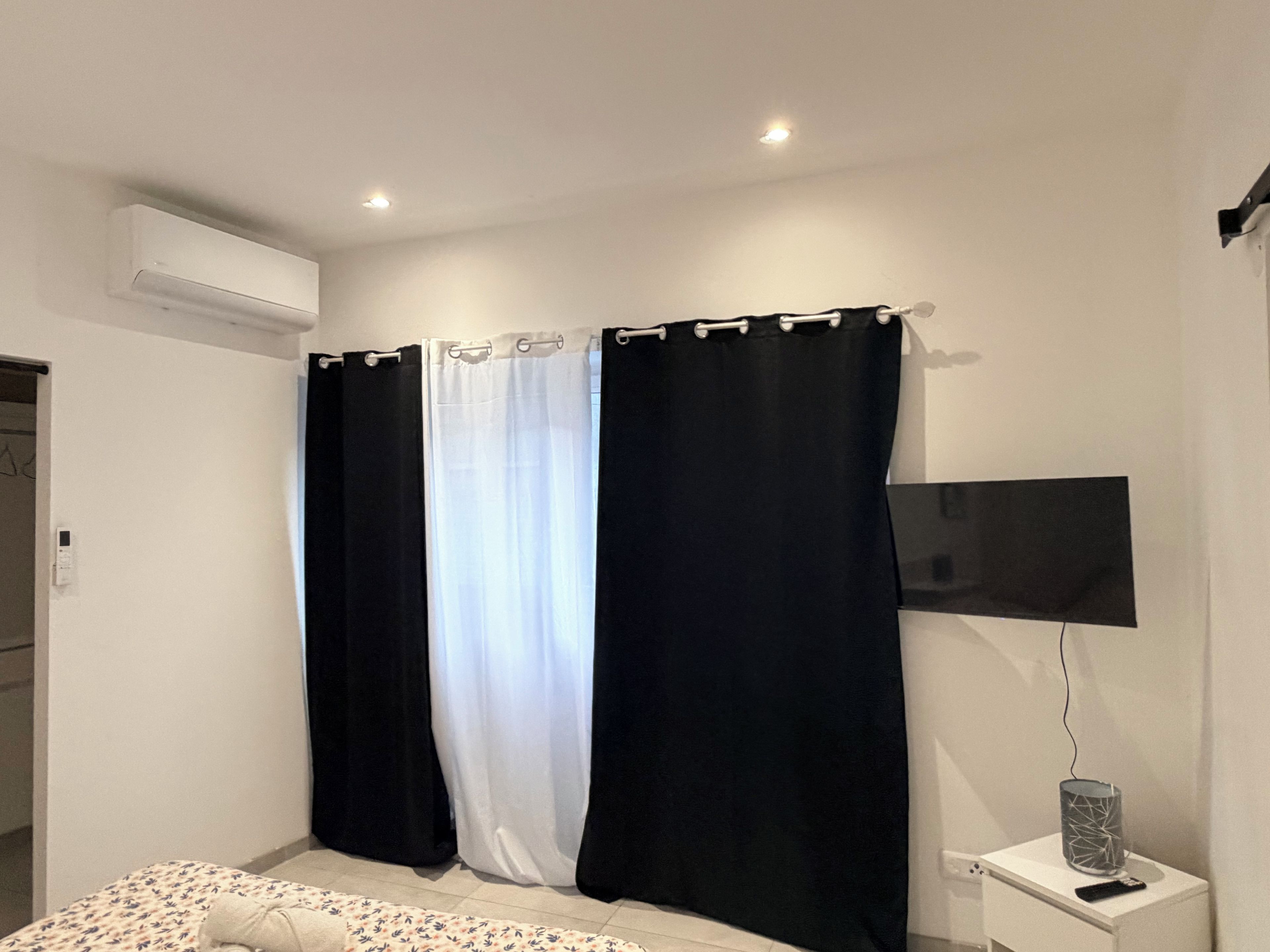 Une chambre à coucher avec un lit, un téléviseur posé sur une table de chevet et une fenêtre ornée de rideaux noirs et blancs.