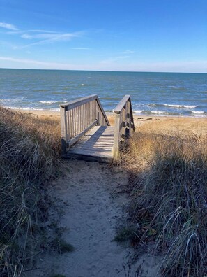 A wooden boardwalk leading to the beach with sandy path and grassy dunes. - Walk to beach, private patio! (Eastham)