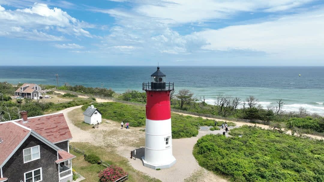 Ein Leuchtturm mit rotem und weißem Turm, umgeben von Grün und einem Strand.