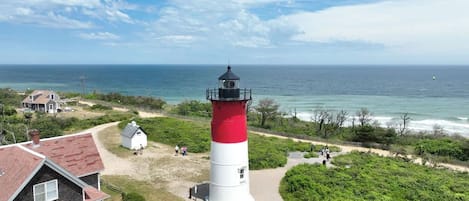 A lighthouse with a red and white structure, surrounded by greenery and a beach.