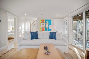 A modern living room with a white sofa, two blue patterned pillows, a wooden coffee table, and a colorful abstract painting on the wall.