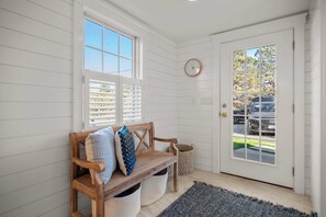 A clean, white-walled entryway with a bench, a door with a window, and a wall clock.