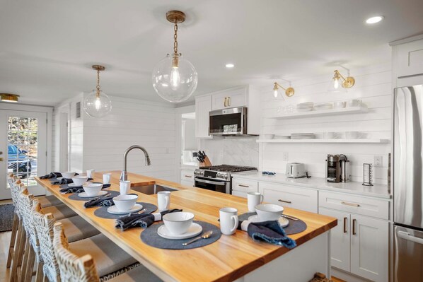 A modern kitchen with a long island, stainless steel appliances, and pendant lighting. - Walk to beach, private patio! (Eastham)