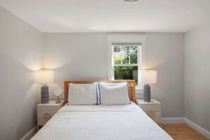 Un dormitorio con una cama grande, dos mesitas de noche, una ventana con vistas a zonas verdes y una lámpara en el techo.
