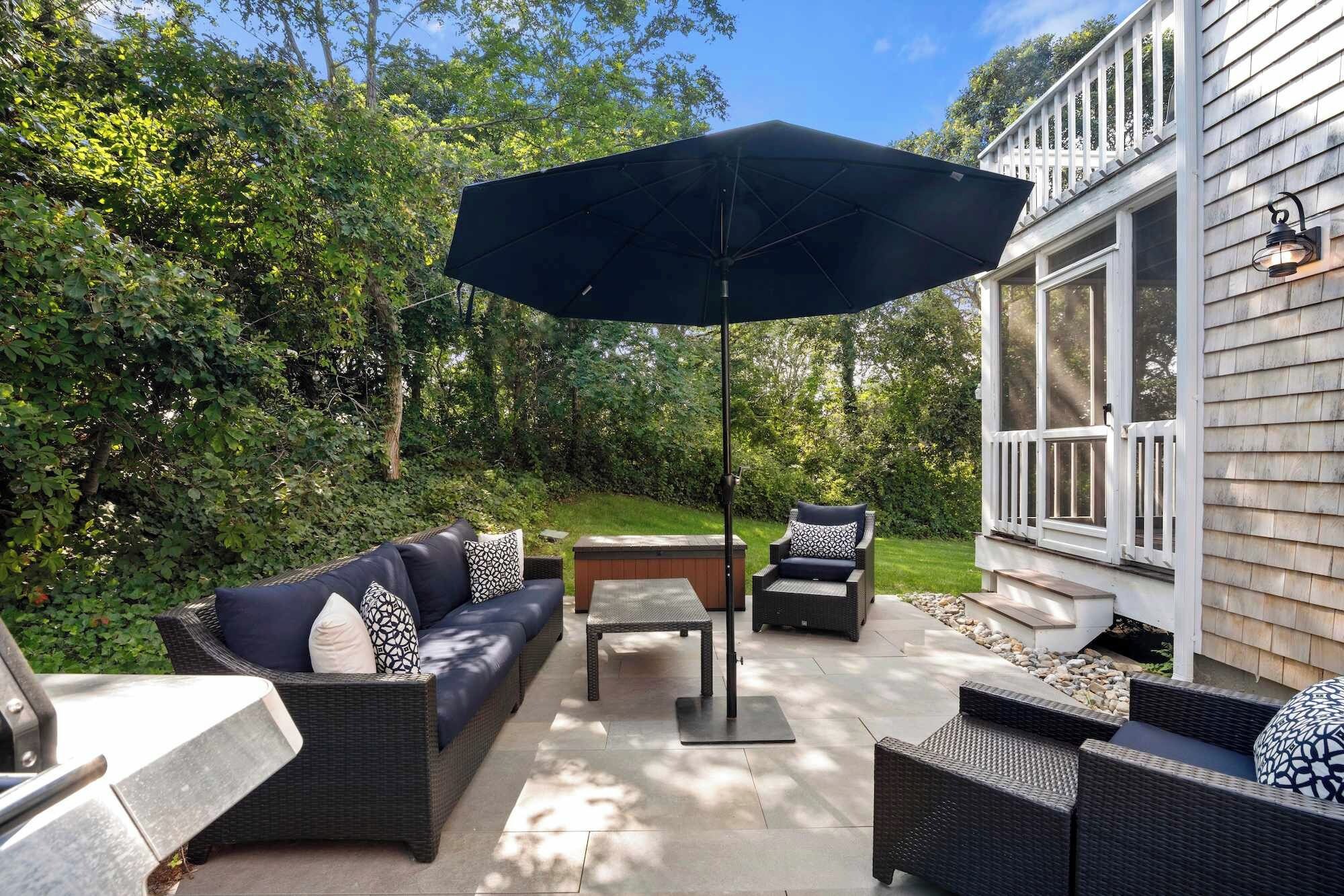 An outdoor patio with wicker furniture, a table, and a large umbrella.