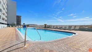 Piscina com deck revestido em azulejos, escada de metal e cadeiras de descanso.