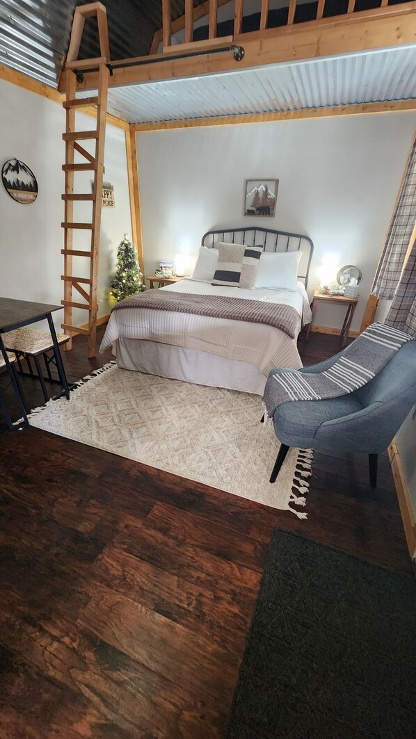 Un dormitorio acogedor con cama, una silla, una mesita, una escalera y un árbol de Navidad.
