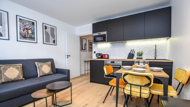 A modern living room with a sofa, coffee table, and dining area with chairs. - Welcoming Apartment - 1br/4p - Arc de Triomphe (Paris)